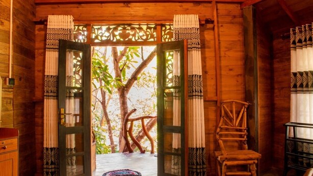 A wooden cabin with a large open doorway leading to a natural area with trees. - Dudley Nature Resort  (Habarana)