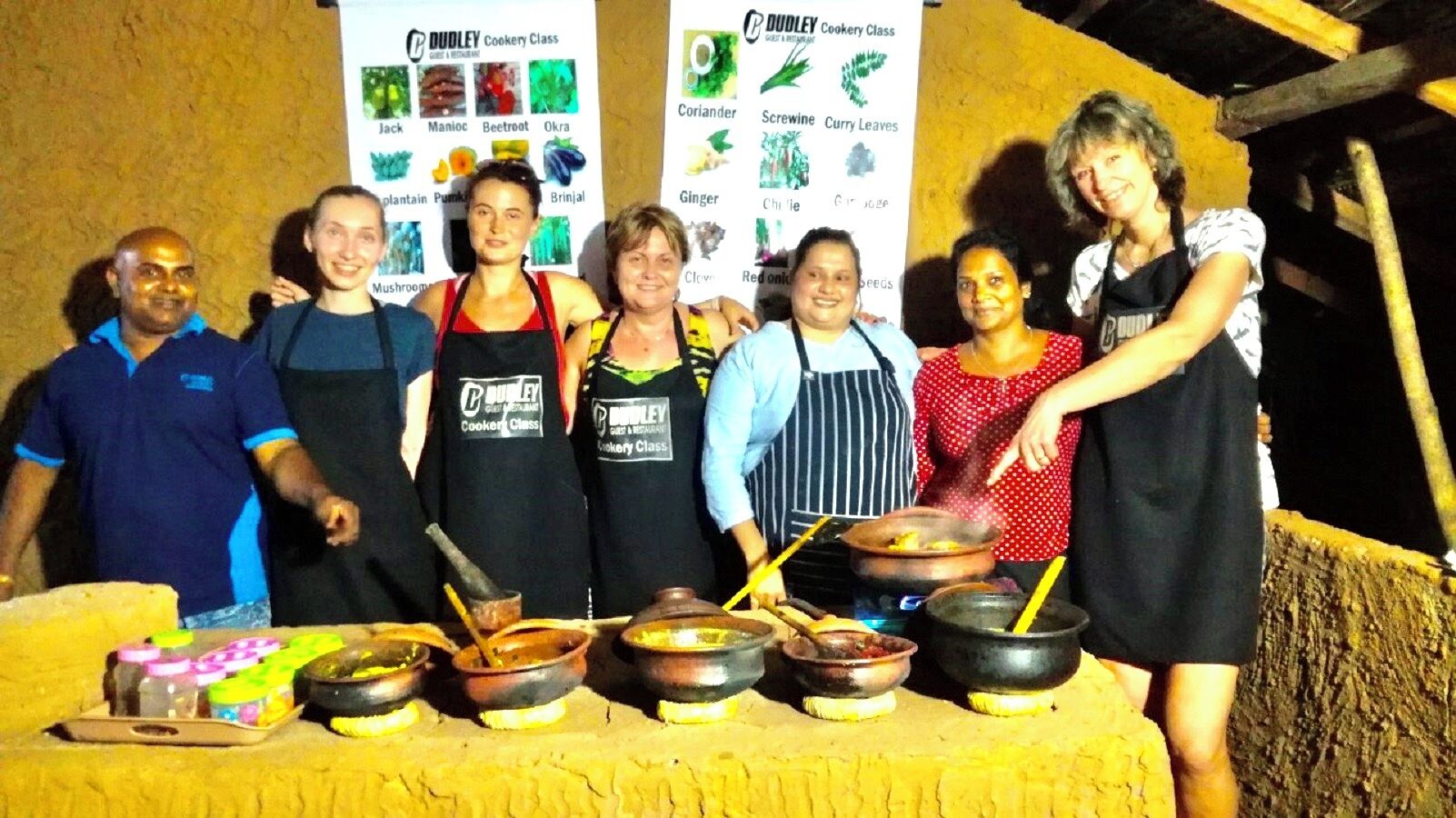 A group of people standing in front of a cooking class banner with various vegetables listed.