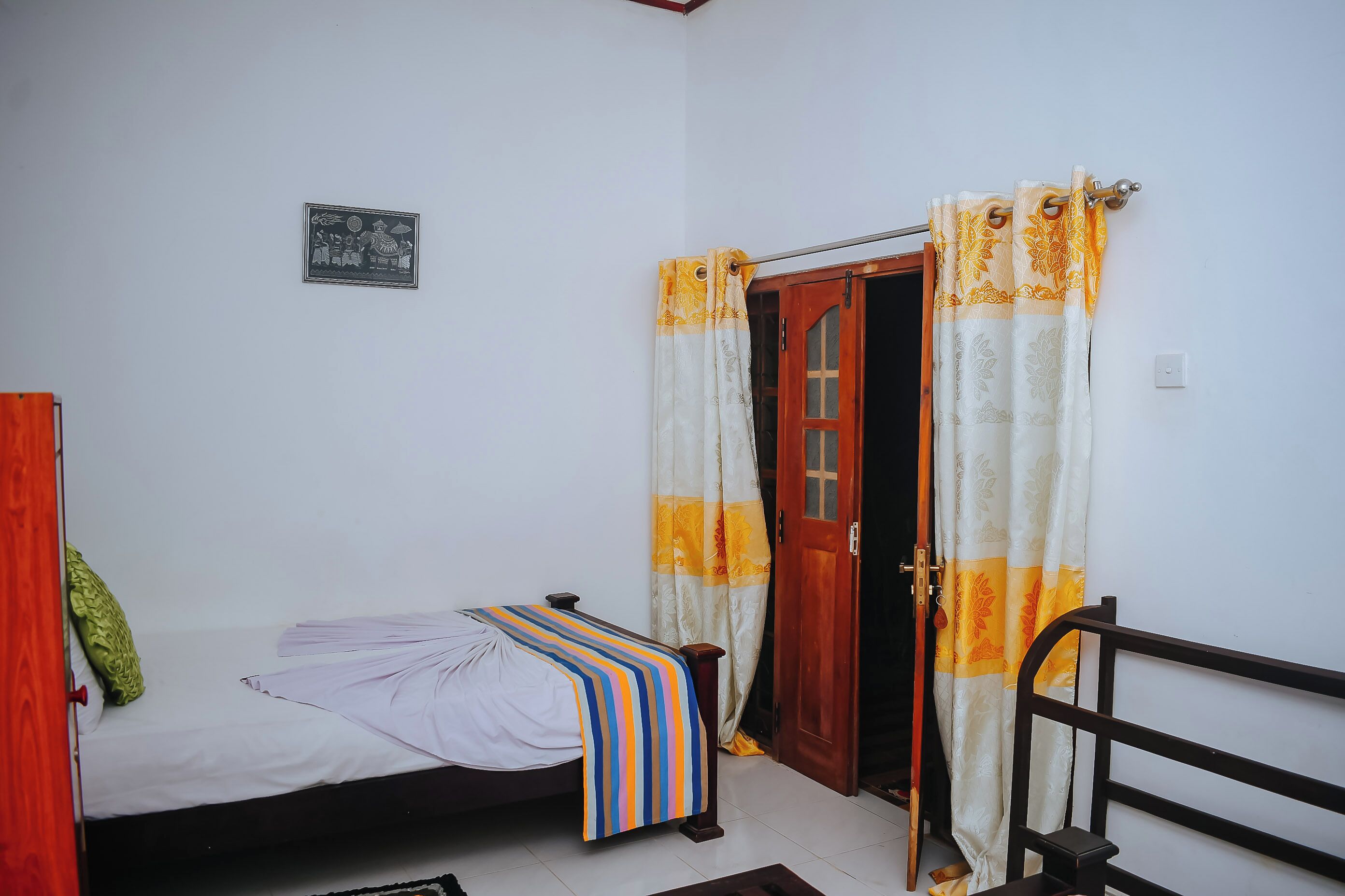 A small, single-bed room with a wooden door, a curtain, and a small framed picture on the wall.