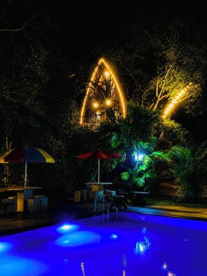 A pool area with a glowing structure resembling a house, surrounded by lush greenery and outdoor seating. - Dudley Nature Resort  (Habarana)