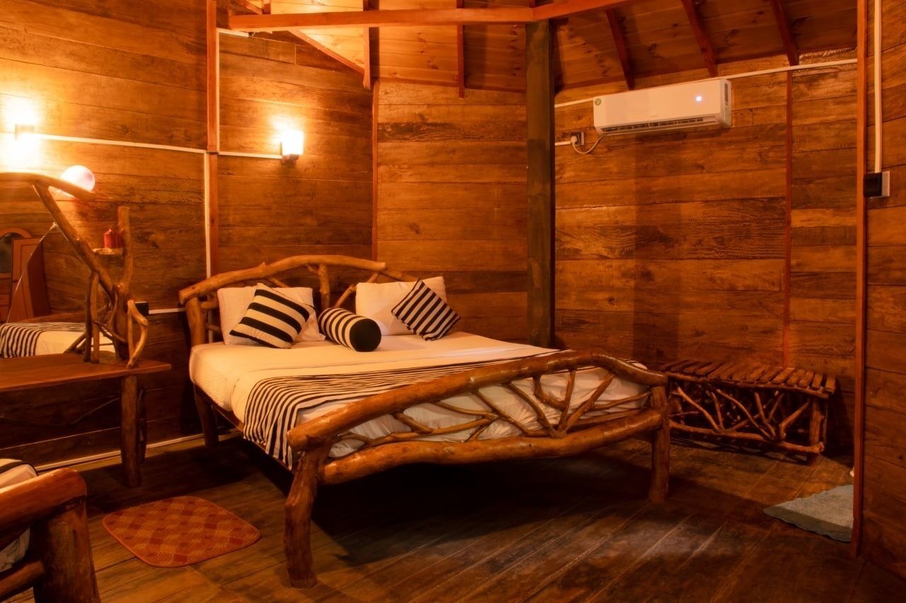 Een houten kamer met een bed, een houten stoel, een kleine tafel en een luchtverwarmer aan de muur.