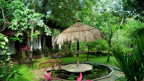 A garden with a thatched umbrella, a pond, and a wooden bench. - Dudley Nature Resort  (Habarana)