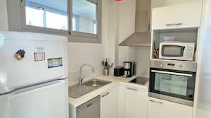 A compact kitchen with a refrigerator, microwave, oven, sink, and a window above the sink. - Apartment T2 - 4 people - City center and beach - Sea view - Air conditioning - WiFi - Sainte-Maxime (STE MAXIME)