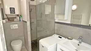 A bathroom with a toilet, a shower, a sink, and a mirror.