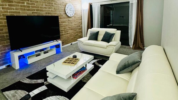 Un salon moderne avec un mur en briques, un téléviseur à écran plat, un canapé blanc et une table basse.