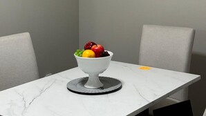 Un coin repas avec une table en marbre, un saladier rempli de fruits et une citation encadrée accrochée au mur.