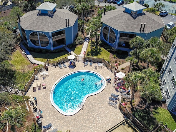 A pool area with a circular pool surrounded by lounge chairs and umbrellas, adjacent to two blue buildings with a unique octagonal roof design.