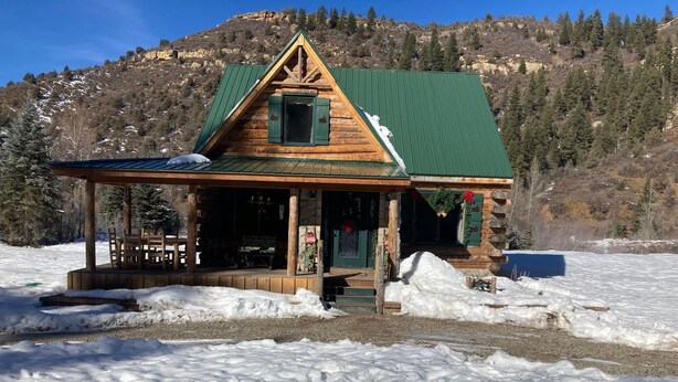 A log cabin with a green roof, a porch, and a mountain backdrop. - Bear Creek Hideaway Log Cabin on River Fishing & WiFi on Kebler Pass (Somerset)