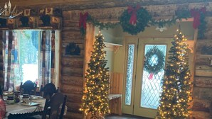 A cozy log cabin interior with a dining area, two decorated Christmas trees, and a fireplace. - Bear Creek Hideaway Log Cabin on River Fishing & WiFi on Kebler Pass (Somerset)