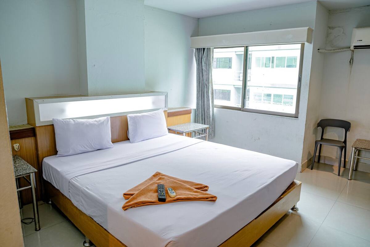 Quarto de hotel com cama grande, uma mesinha, uma cadeira e janela com vista para edifícios.