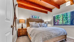 A bedroom with a wooden bed, a nightstand, a lamp, and a window with a view of trees.