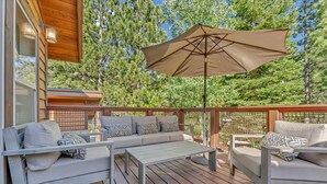 A wooden deck with a sofa and chairs, an umbrella, and a wooden railing.
