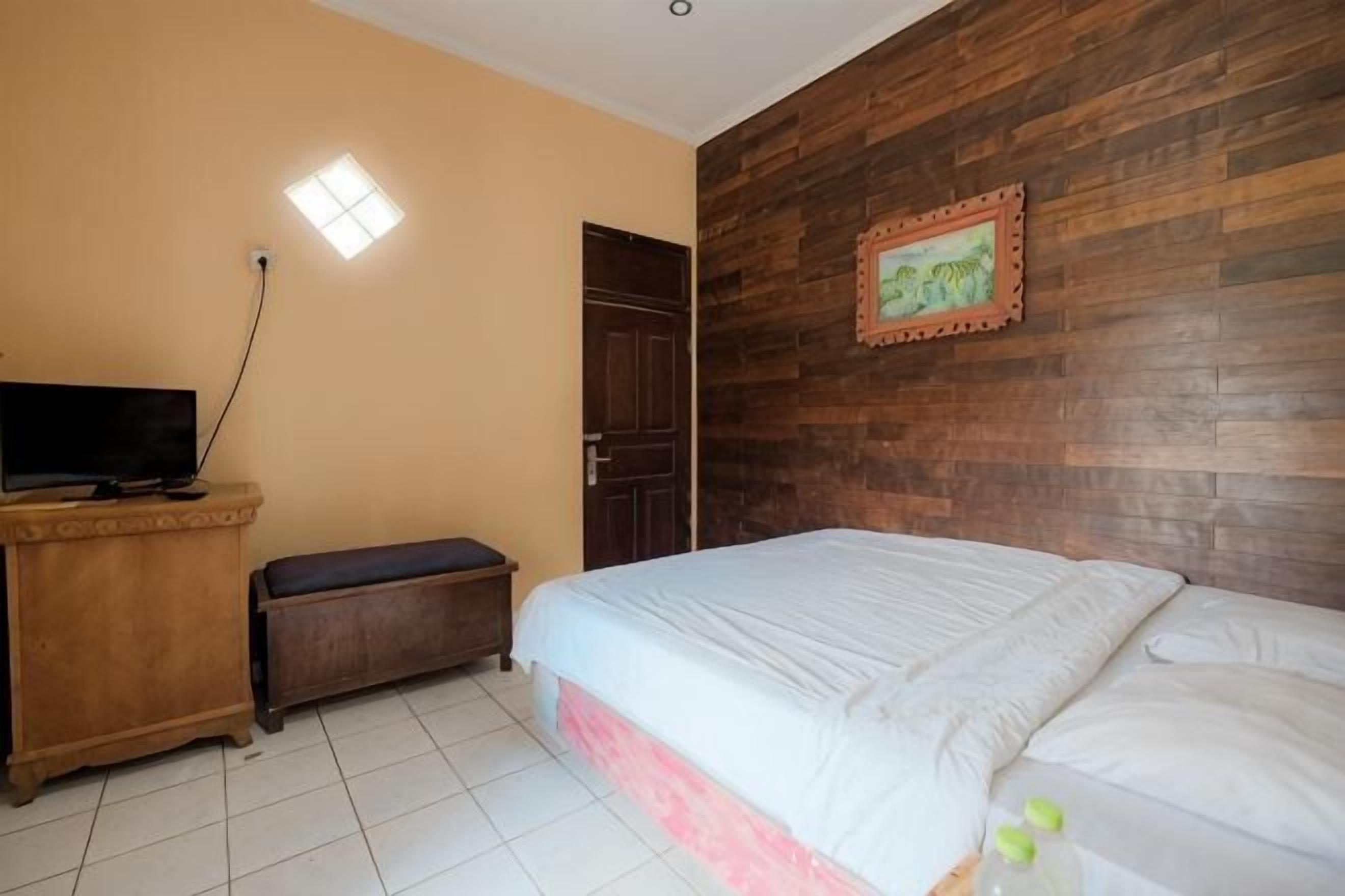 A bedroom with a bed, a wooden wall, a door, a television, and a small bench.