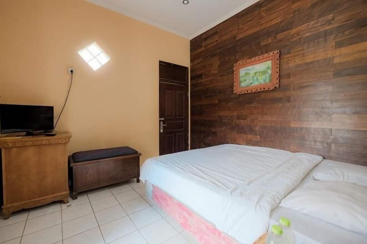 A bedroom with a bed, a wooden wall, a door, a television, and a small bench.