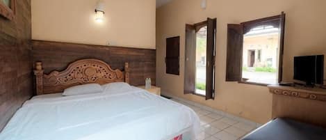 A bedroom with a wooden headboard, a bed, a nightstand, a bench, a TV, and a window with an open door.