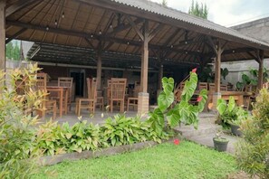A covered outdoor seating area with wooden furniture and potted plants. - Pelangi Homestay RedPartner (Bali)