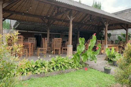 A covered outdoor seating area with wooden furniture and potted plants.. Pelangi Homestay RedPartner
