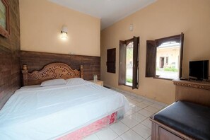 A bedroom with a wooden bed, bedside tables, a bench, a TV, and a window. - Pelangi Homestay RedPartner (Bali)