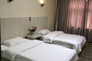 Una habitación de hotel con dos camas, una mesita de noche con un florero y una ventana con cortinas.