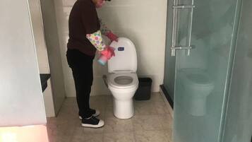 A person cleaning a toilet in a bathroom with a glass shower door.