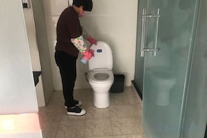 A person cleaning a toilet in a bathroom with a glass shower door.