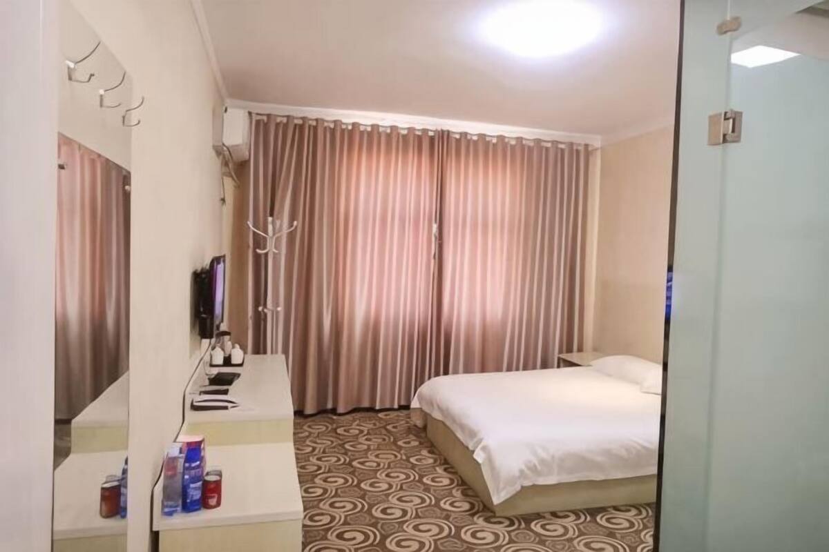 Quarto de hotel com uma cama, uma escrivaninha com espelho, televisão e janela com cortinas.