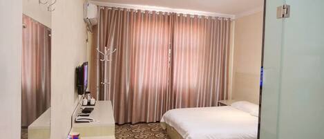 Habitación de hotel con cama, mesita de noche, espejo, televisor y cortina.