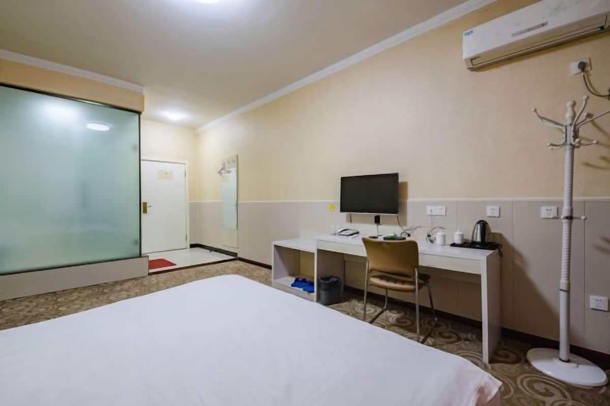 Quarto de hotel com cama, escrivaninha com computador, cadeira, televisão e um cabideiro.