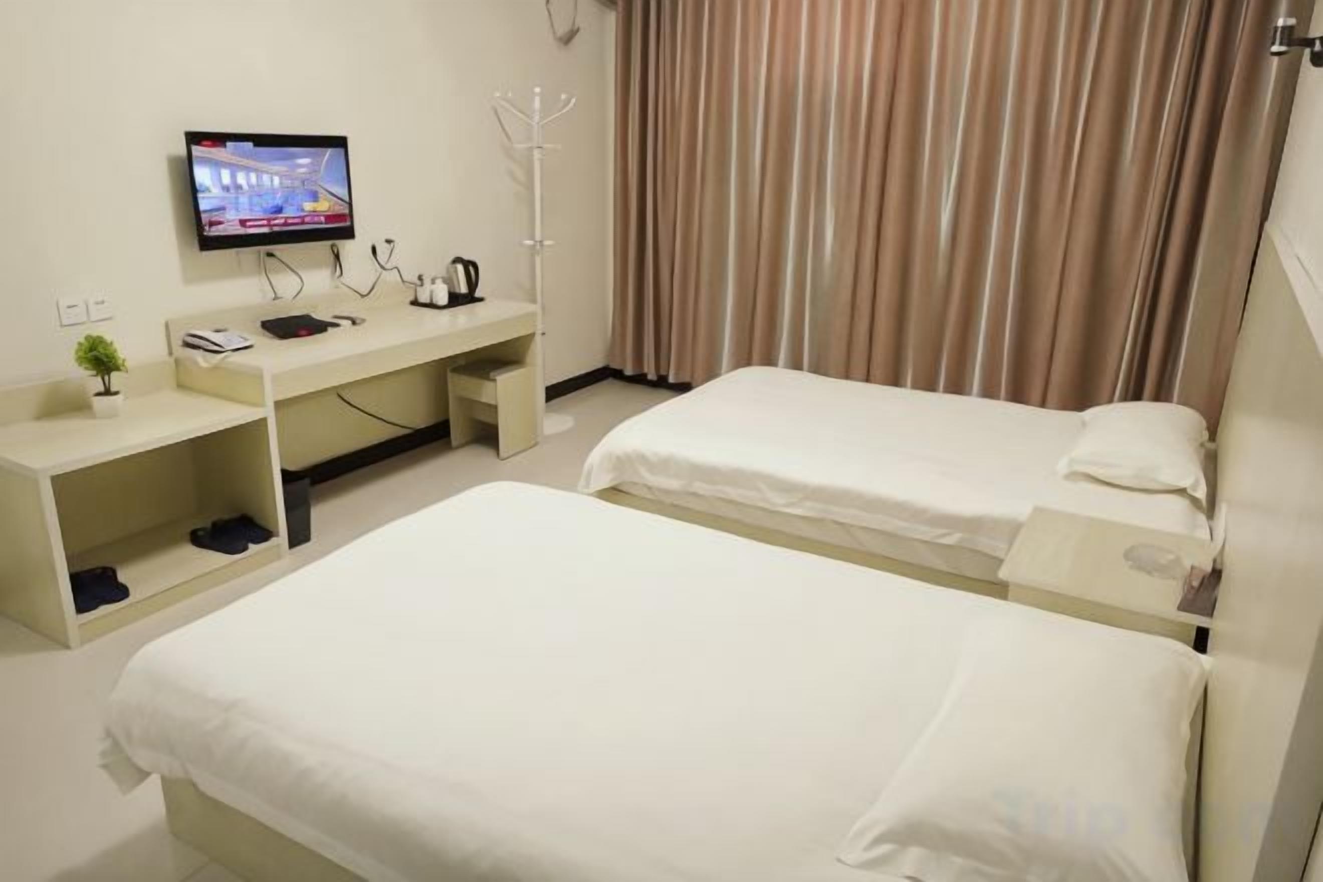 Camera d'albergo con due letti, una scrivania con televisore, un attaccapanni e una finestra con tende.