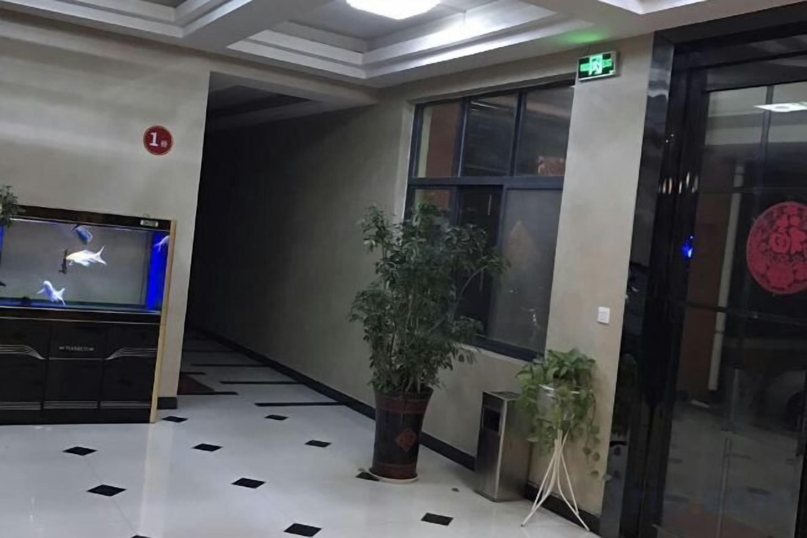 A lobby with a reception desk, a potted plant, a staircase, and an elevator.