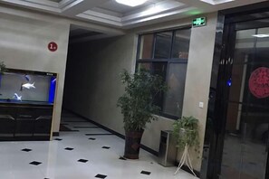 Vestíbulo con mostrador de recepción, planta en maceta, escalera y ascensor.