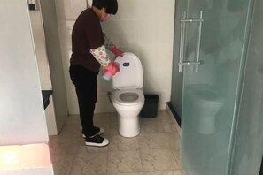 A person cleaning a toilet in a bathroom with a glass partition and a trash bin. - Civil rights Holiday Inn (Minquan)