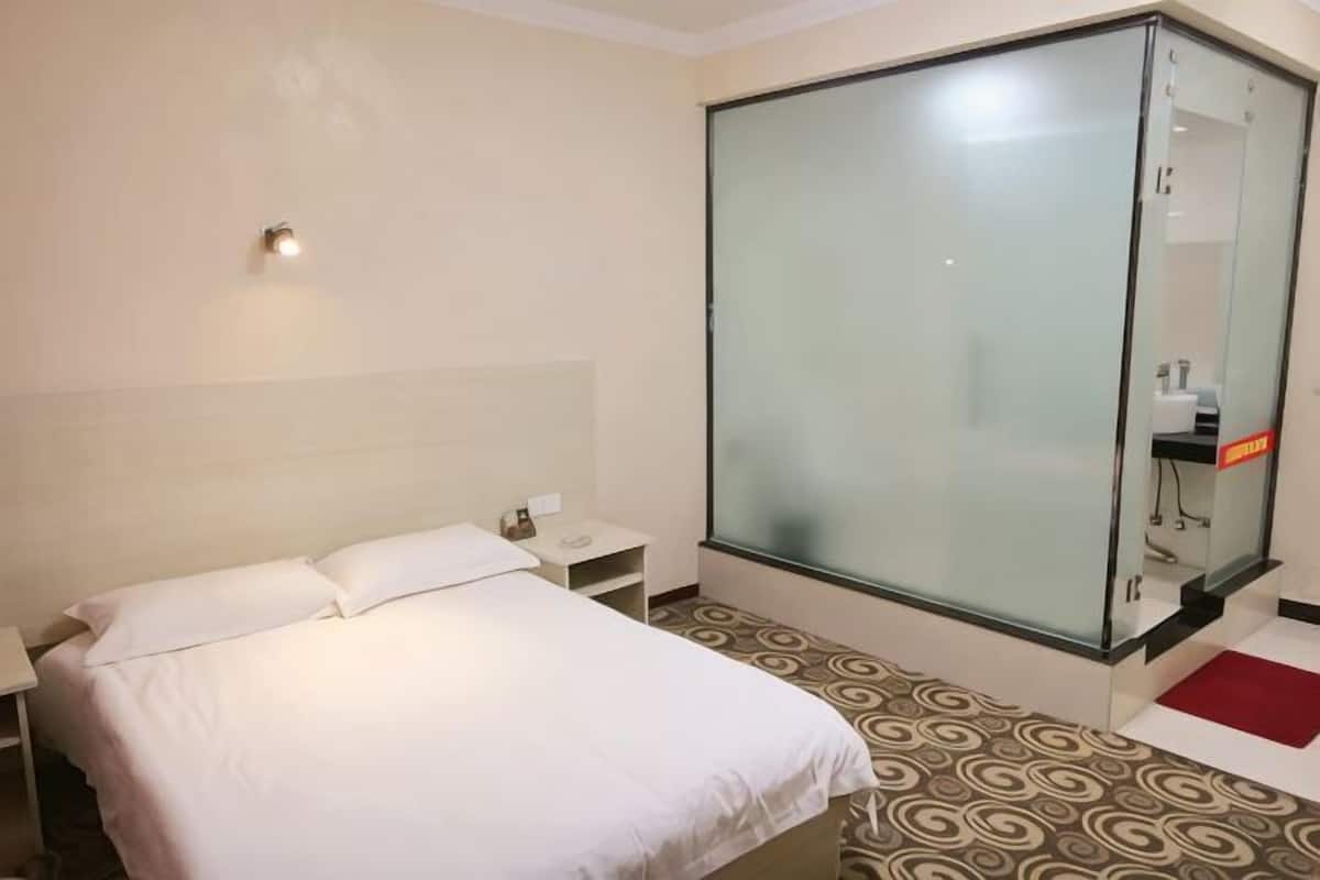 Une chambre dâhĂŽtel avec un lit, une table de chevet, une cabine de douche en verre et un sol Ă motifs.