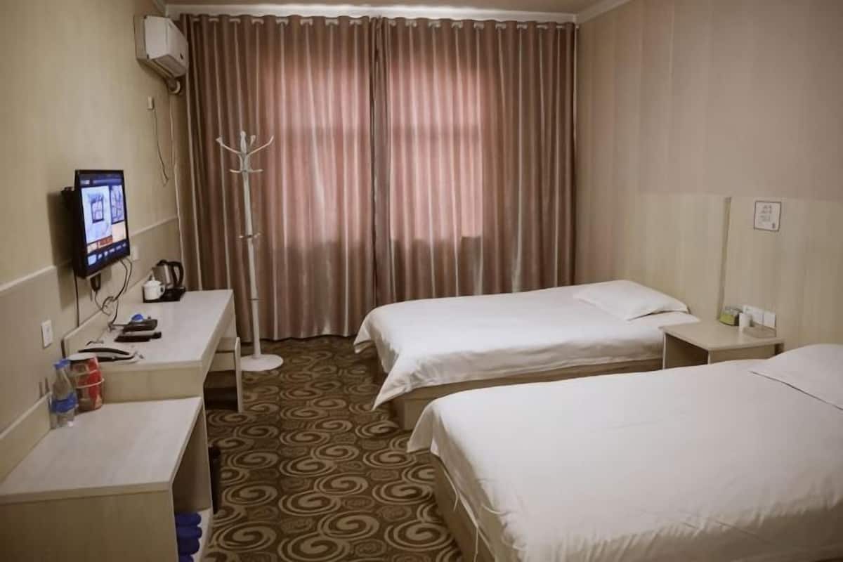Quarto de hotel com duas camas, uma escrivaninha com computador, um cabideiro e uma janela com cortinas.