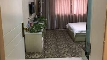 A hotel room with a bed, a small bedside table, a TV, and a curtain.