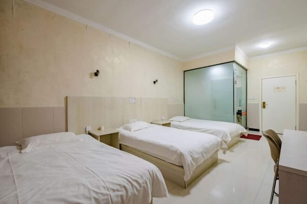Quarto de hotel com três camas, uma escrivaninha, uma cadeira e um espelho.