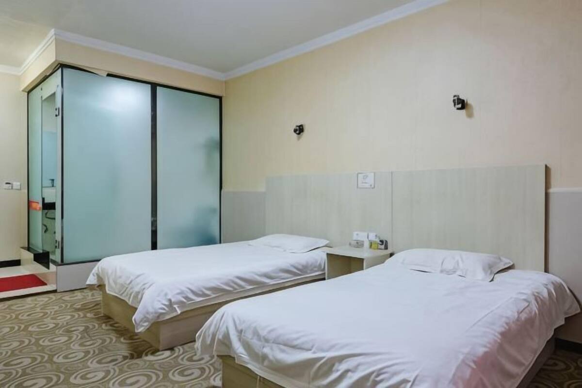 Quarto de hotel com duas camas de solteiro, um guarda-roupa, uma mesa de cabeceira e uma pequena escrivaninha.