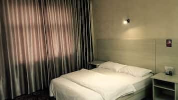 A hotel room with a bed, curtains, a nightstand, and a wall-mounted light.