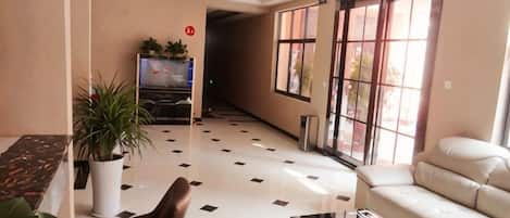 A hotel lobby with a sofa, a chair, a coffee table, a TV, and a potted plant.