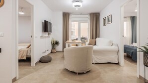 A modern, well-lit living room with a sofa, ottoman, and a flat-screen TV mounted on the wall. - 2 bed Apt, 2 Bath 4px seaside (Cádiz)