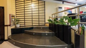 A hotel lobby with a curved staircase, a potted plant, and a large window with horizontal blinds. - Hotel Sogo Cainta (Cainta)