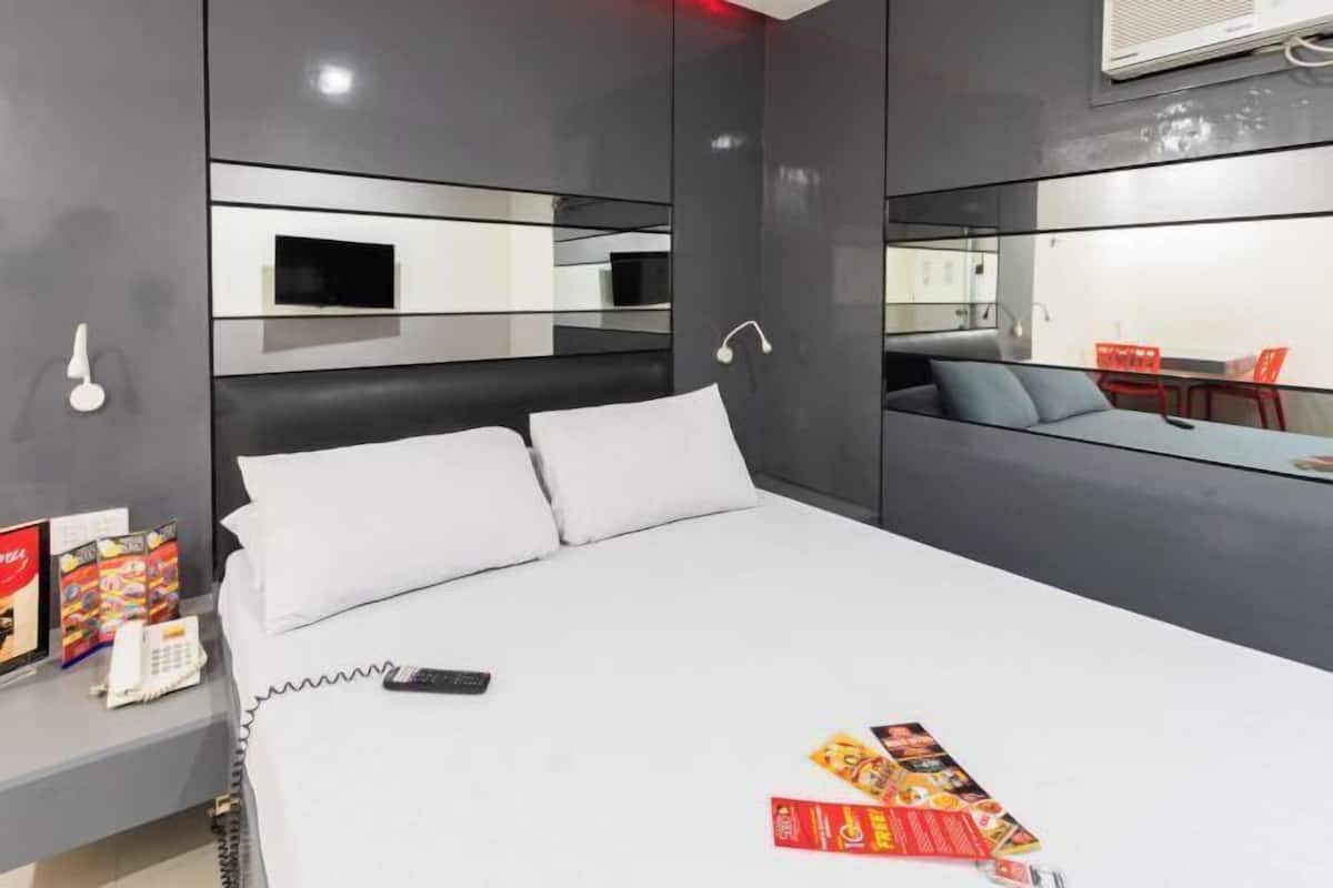 Una habitación de hotel moderna con una cama, mesita de noche y un televisor pequeño.