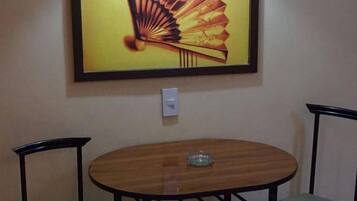 A dining area with a round table and two chairs, a wall-mounted light switch, and a framed artwork above the table.