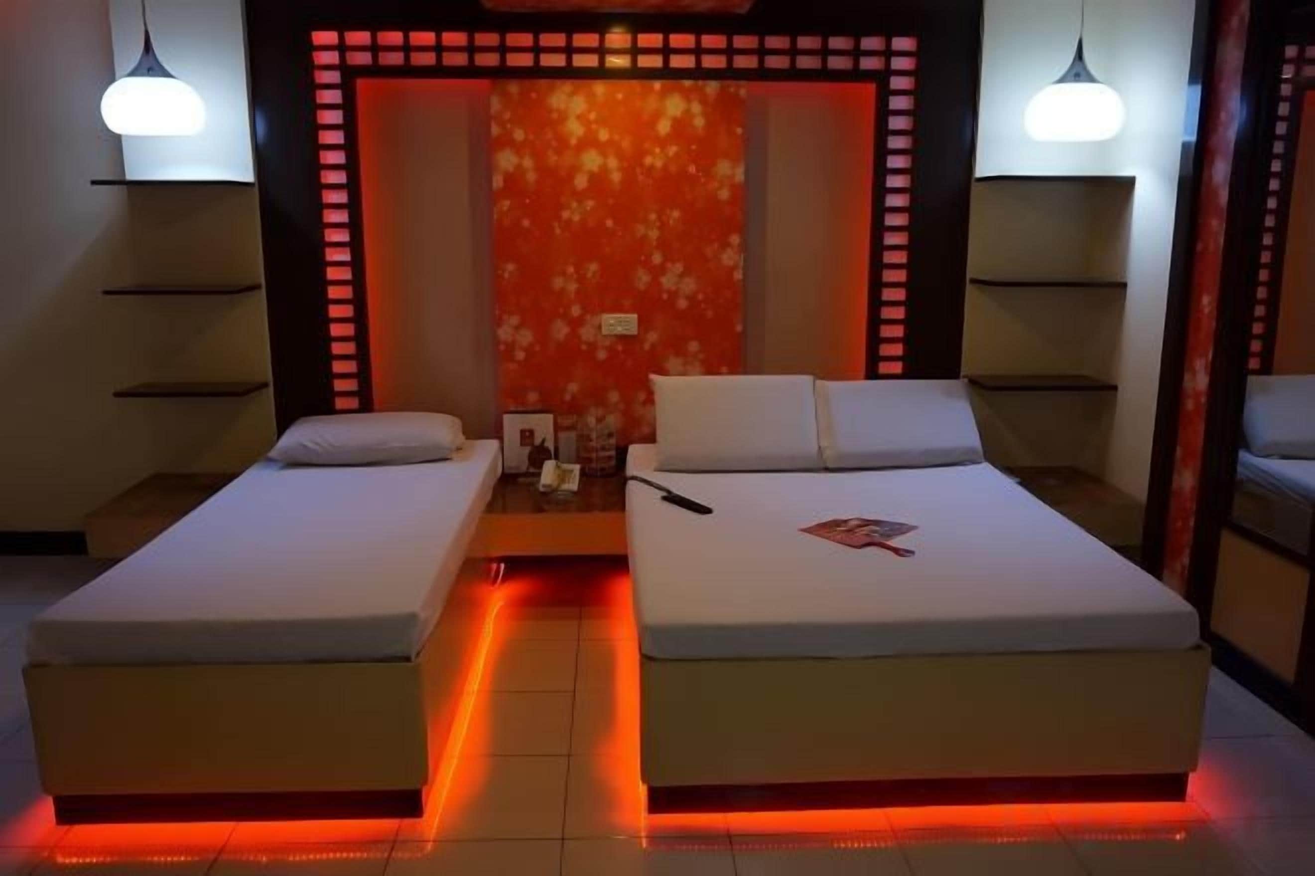 Quarto de hotel com duas camas, parede iluminada em vermelho e luminárias pendentes.