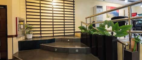 A hotel lobby with a curved staircase, a potted plant, and a wall with horizontal slats.