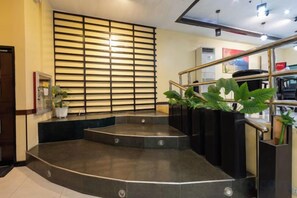 A hotel lobby with a curved staircase, a potted plant, and a wall with horizontal slats. - Hotel Sogo Cainta (Cainta)