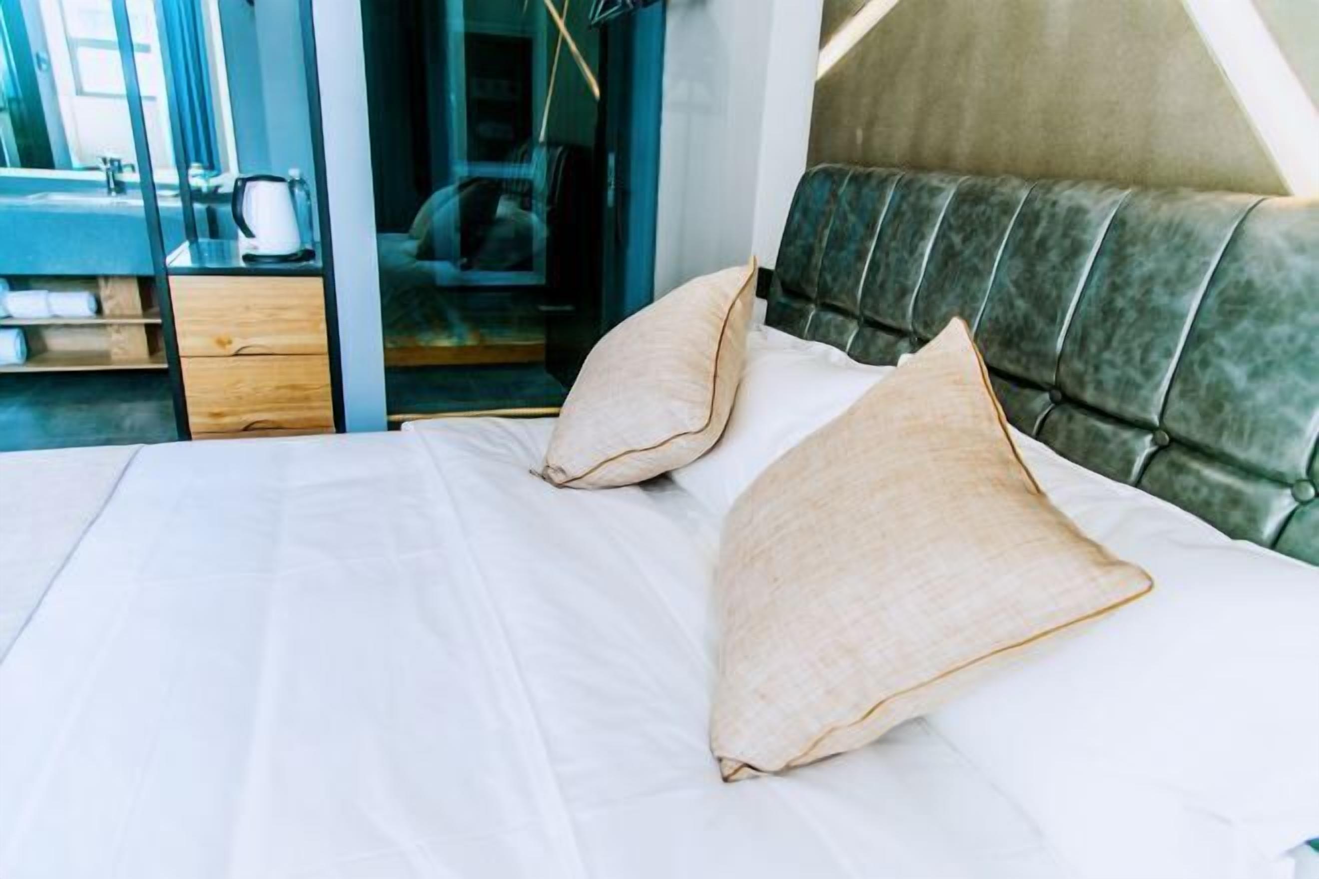 A neatly made bed with two pillows, a wooden nightstand, and a glass door leading to a bathroom.