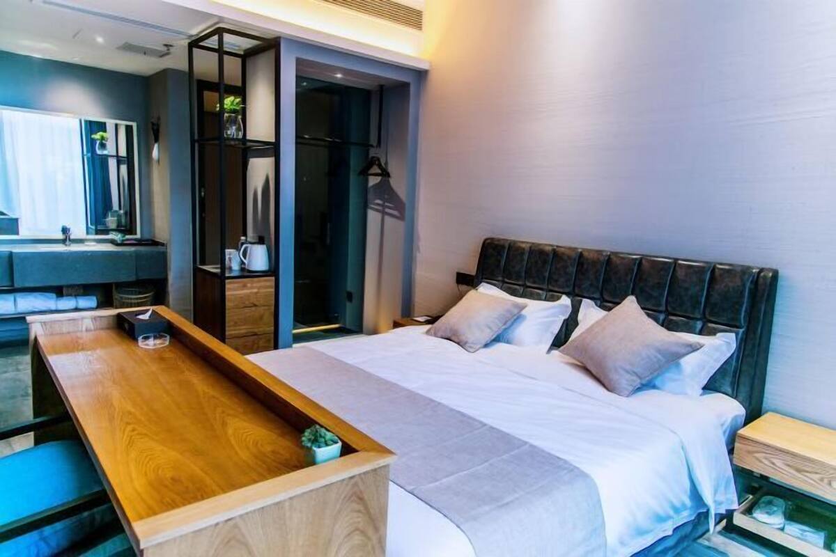 Moderni hotellihuone, jossa on sänky, yöpöytä ja sisäänrakennettu vaatekaappi.