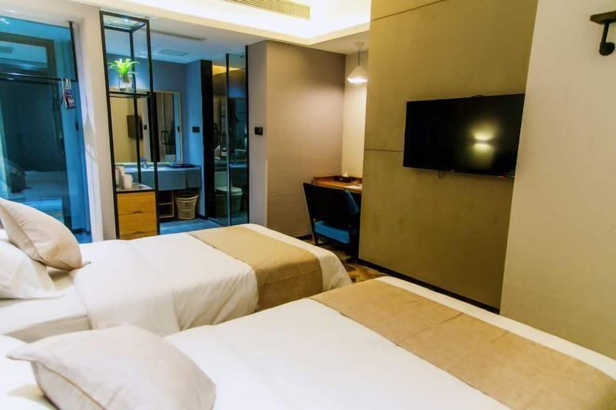 Hotellihuone, jossa on kaksi sänkyä, työpöytä, televisio ja kylpyhuone, joka näkyy lasiovesta.