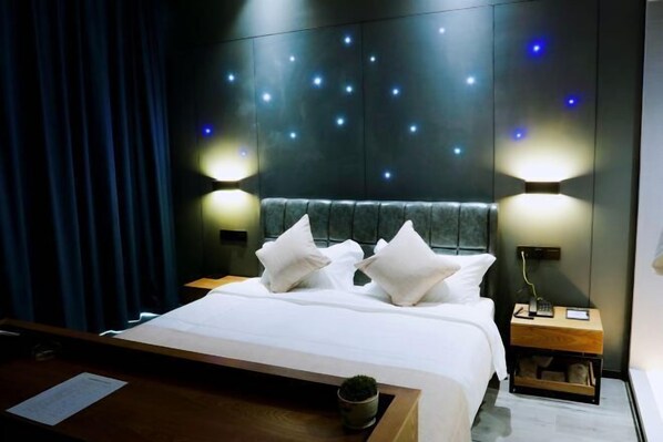 Una habitación de hotel moderna con una cama grande, dos mesitas de noche y una pared con luces que simulan estrellas.